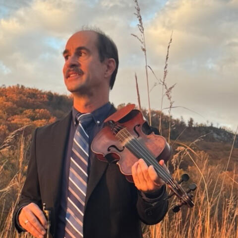 Rex McGee holding a fiddle outdoors in the mountains